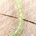 Facettiertes Kugelarmband grüner Peridot auf natürlichem Holzuntergrund, handgefertigte Perlen in elegantem Design.