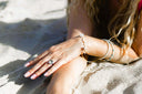 Frau liegt im Sand und zeigt Armband und Ring
