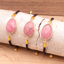 Verstellbares Armband mit Stein-Medaillon in Rosa-Rhodonit Varianten auf Holzuntergrund.
